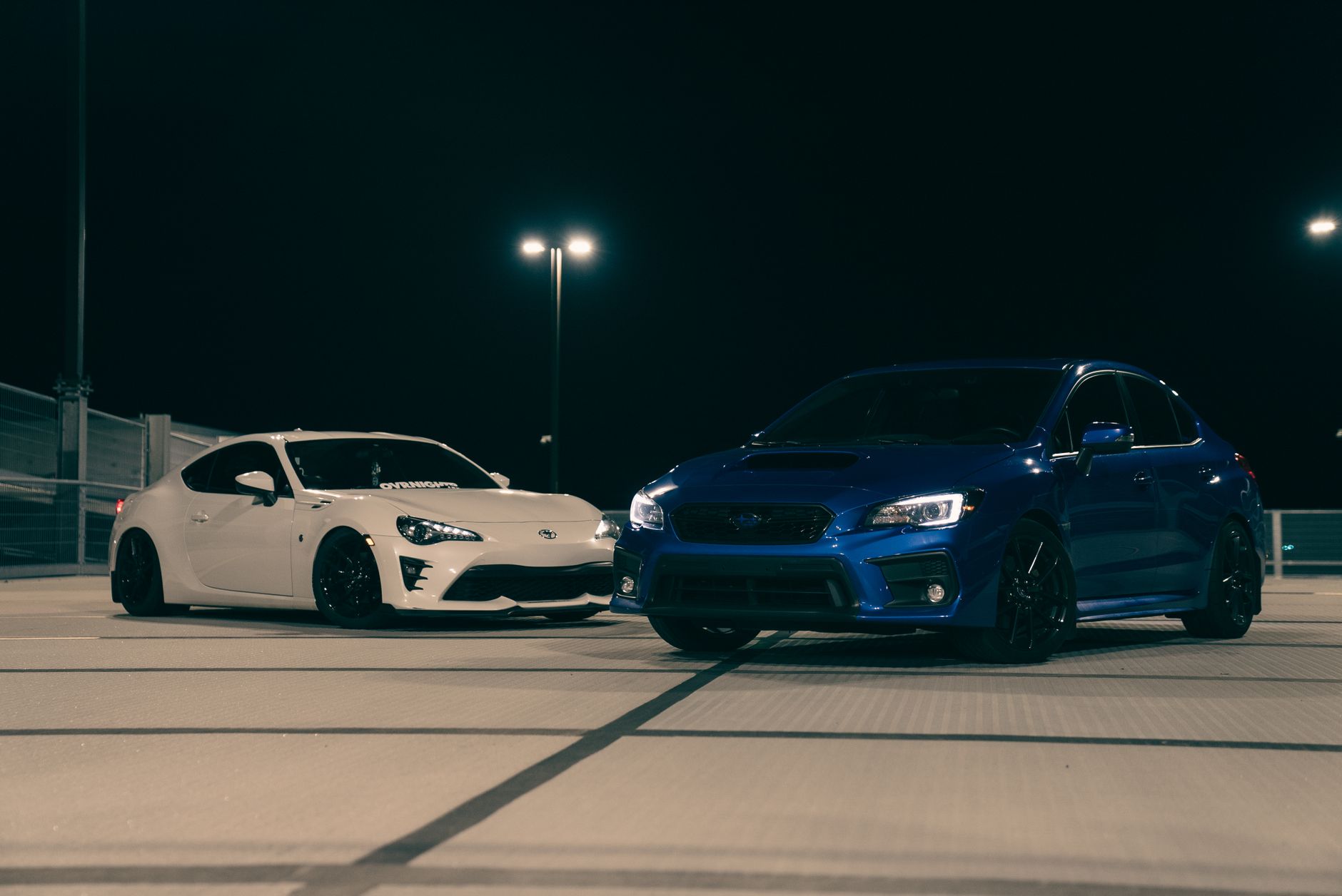 Używana Toyota Corolla czy Auris co wybrać żeby nie żałować po zakupie Biała i niebieska sportowa Toyota stoją nocą na dachu parkingu
