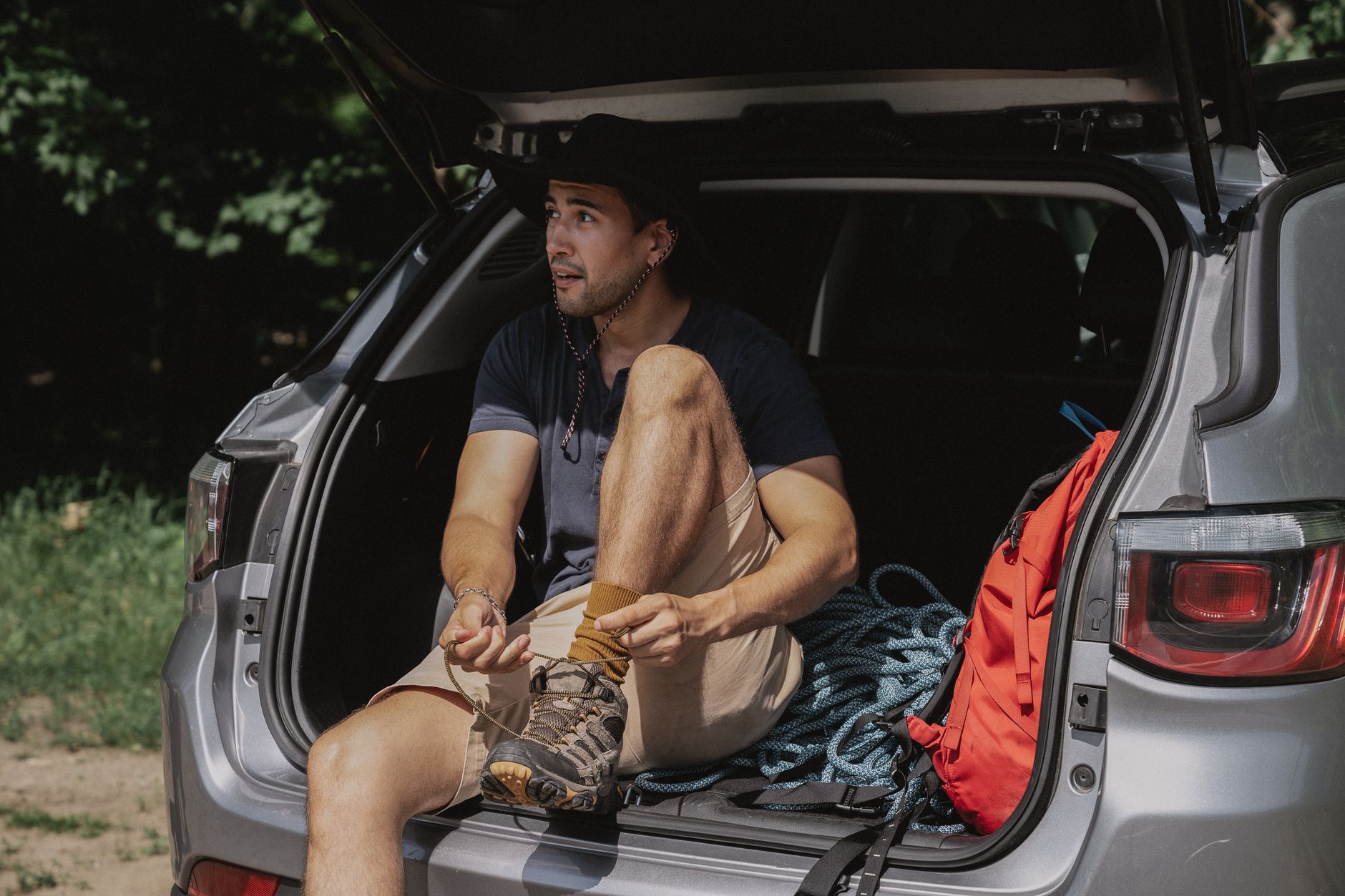 Mężczyzna wiąże buty trekkingowe w bagażniku SUV-a przed podróżą