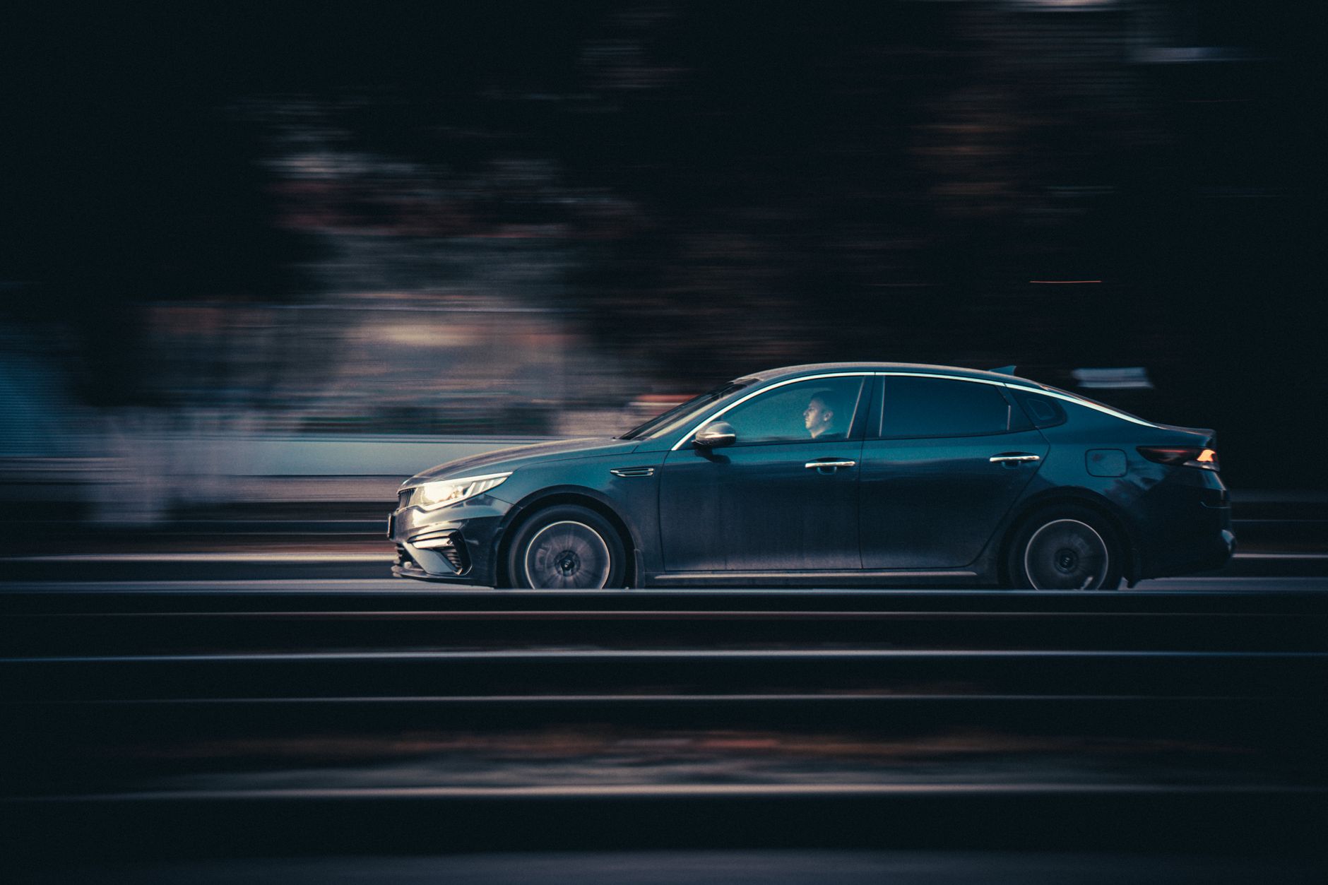 Czarna Skoda Superb jedzie szybko nocą po oświetlonej drodze